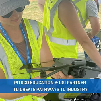Teacher holds a drone while going through Instructor training; She wears a hat, sunglasses and a safety vest.