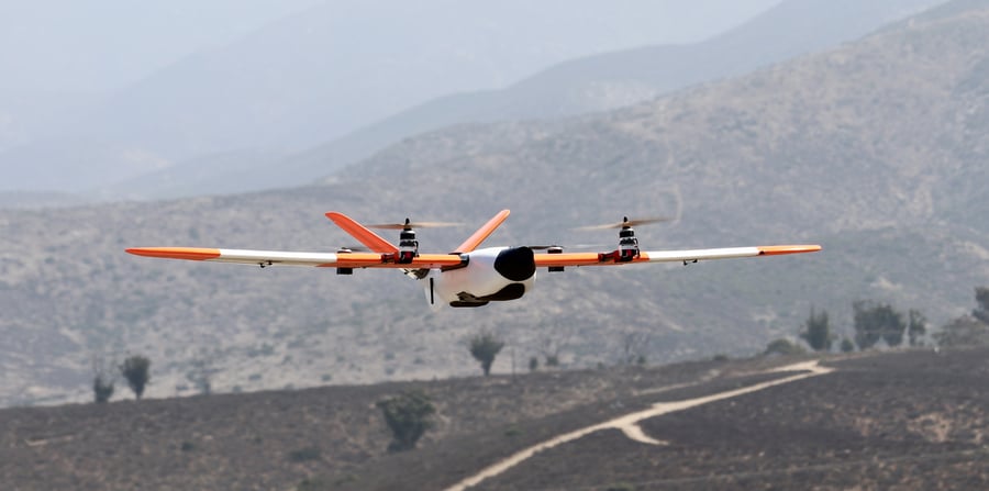 A fixed-wing VTOL drone flying over mountainous terrain