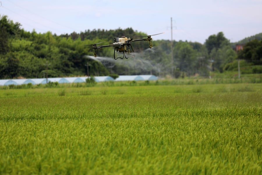 A spray drone applying treatment over a green crop field
